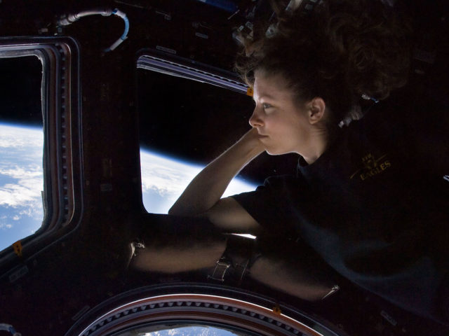 NASA astronaut Tracy Caldwell Dyson, Expedition 24 flight engineer, looks through a window in the Cupola of the International Space Station. A blue and white part of Earth and the blackness of space are visible through the windows.